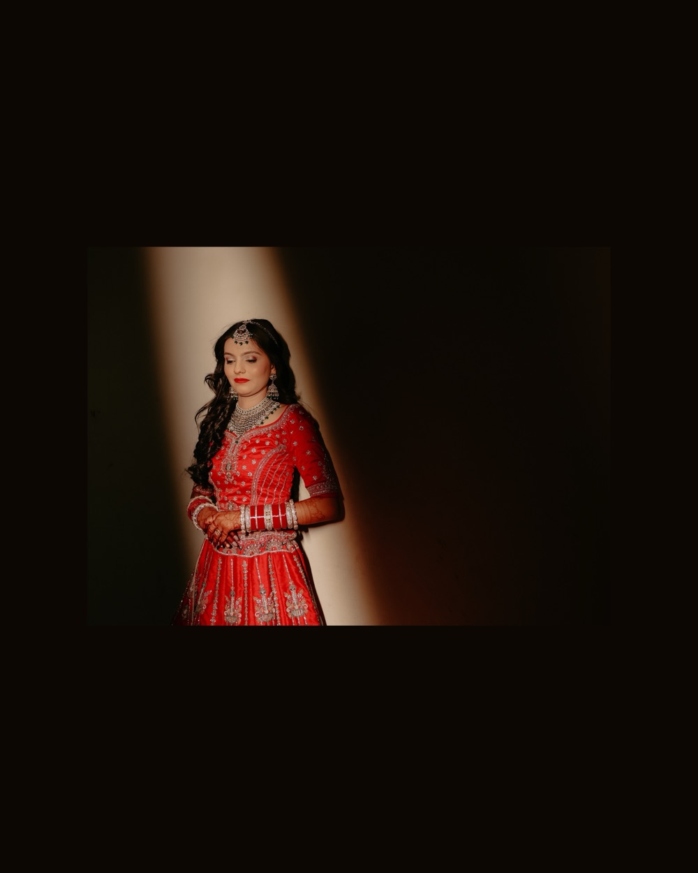 The bride in red standing in a shaft of light against a dark wall