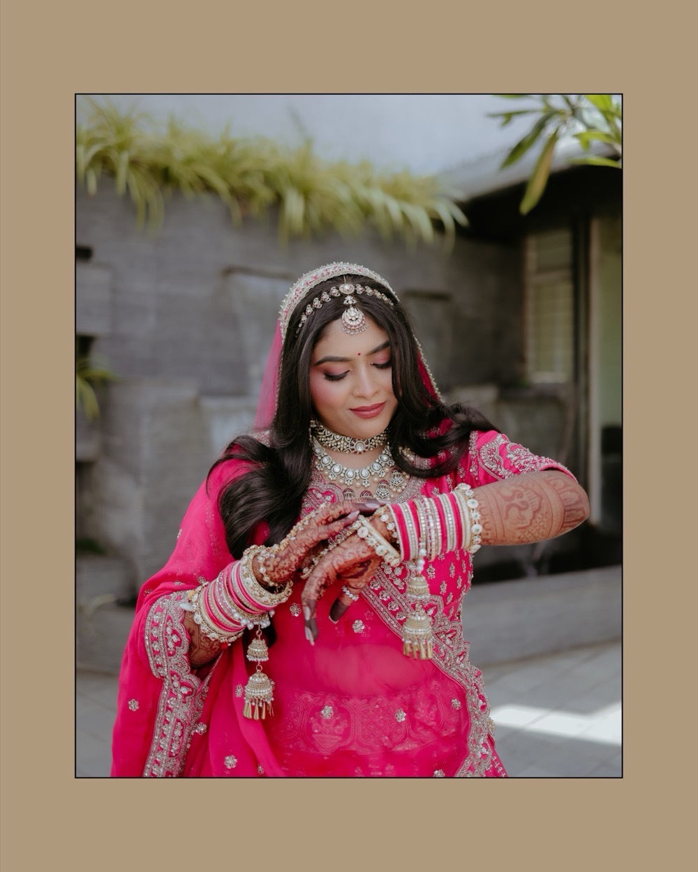 Bridal portrait — the bride looks down at her bangles, framed on a warm ground