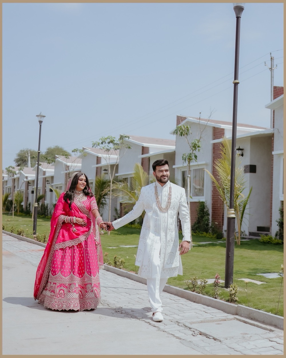 Bride and groom walking hand in hand along a sunlit lane
