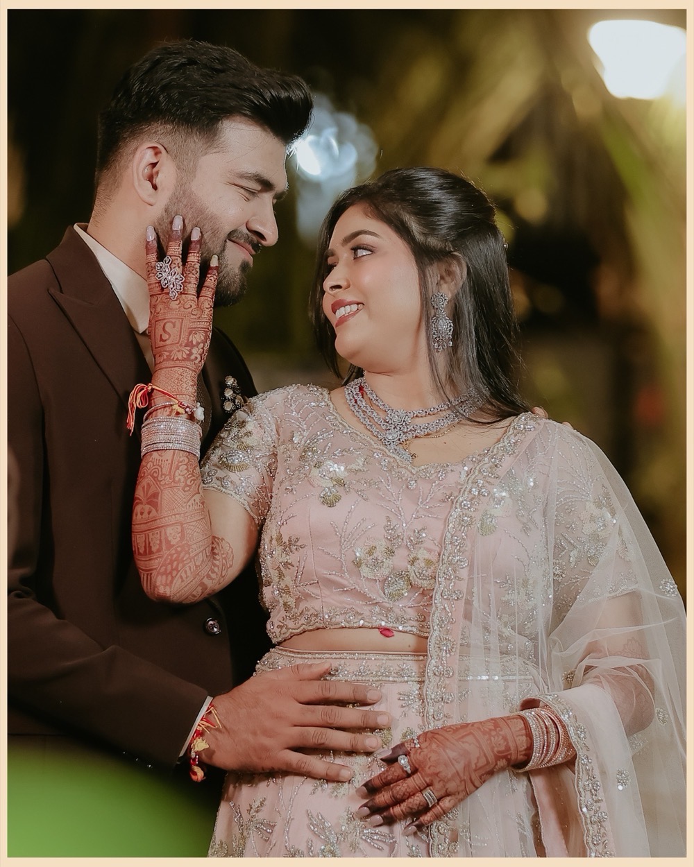 Bride resting her hennaed hand on the groom's cheek as they smile at each other